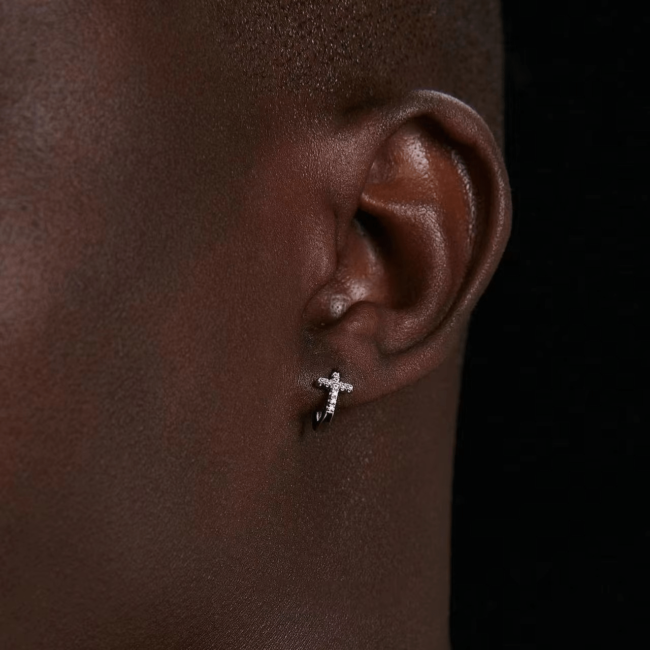 Oreille masculine portant une boucle d’oreille en argent 925, forme anneau avec croix en diamant, fond sombre