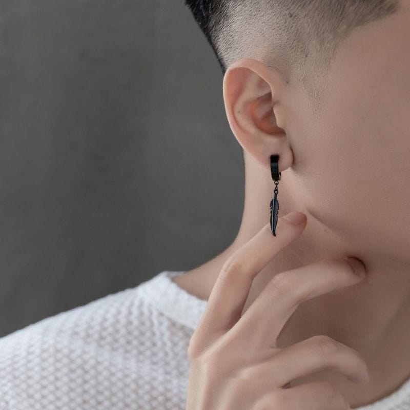 Gros plan sur une boucle d'oreille pendante en acier inoxydable noir avec un motif plume.