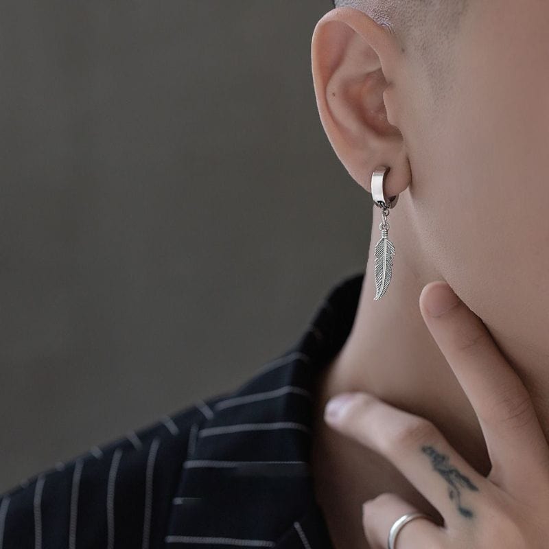 Homme stylé portant une boucle d'oreille pendante en acier inoxydable argenté, modèle plume.