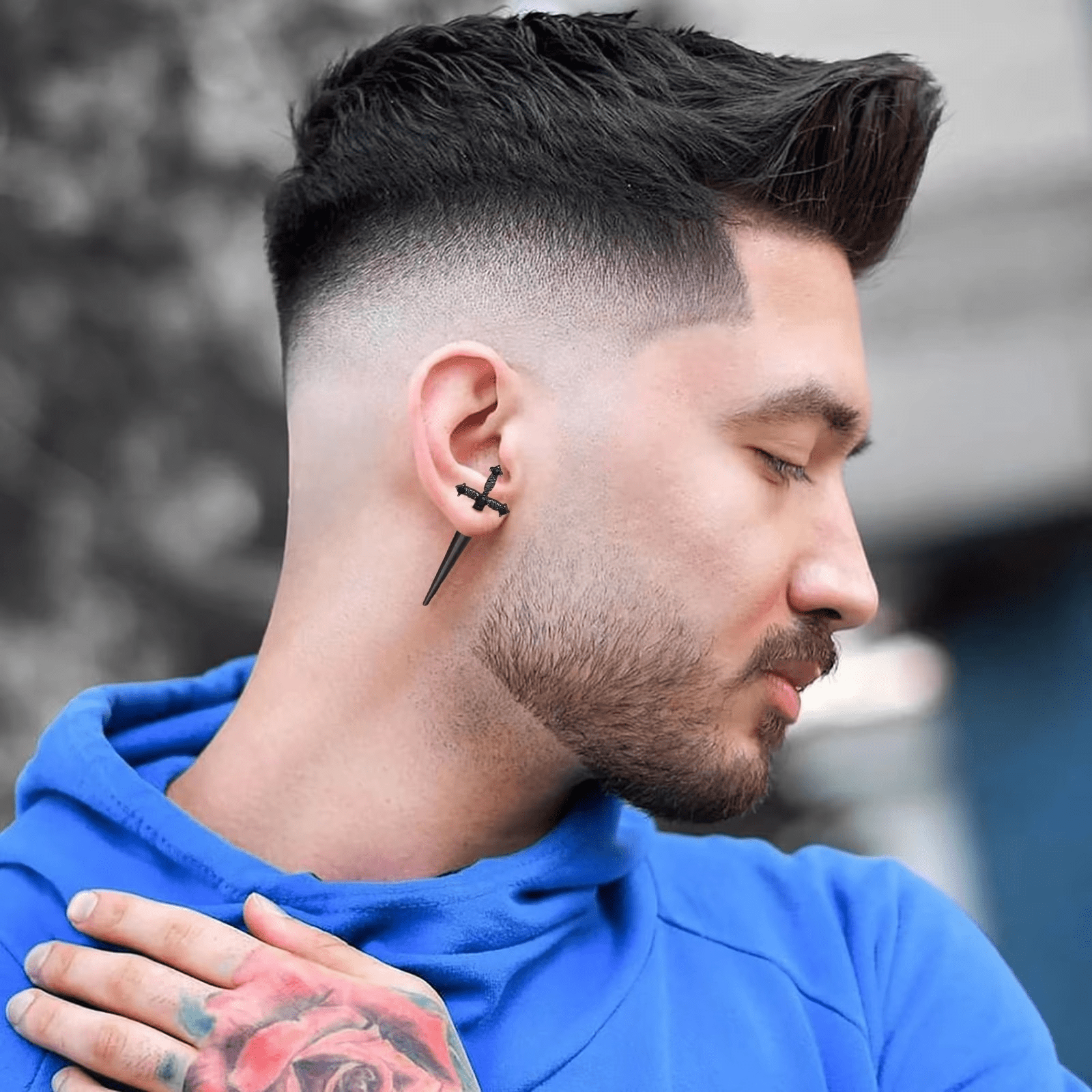 Homme au style moderne portant une boucle d'oreille en forme d'épée, look rebelle et sophistiqué.