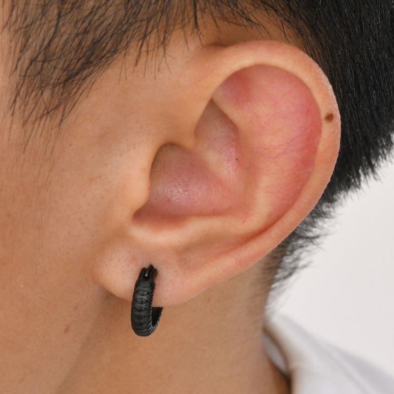 Paire de boucles d'oreilles anneaux pour homme en acier inoxydable noir avec motif serpent discret, portées sur l'oreille pour illustrer leur taille et leur style élégant et masculin.