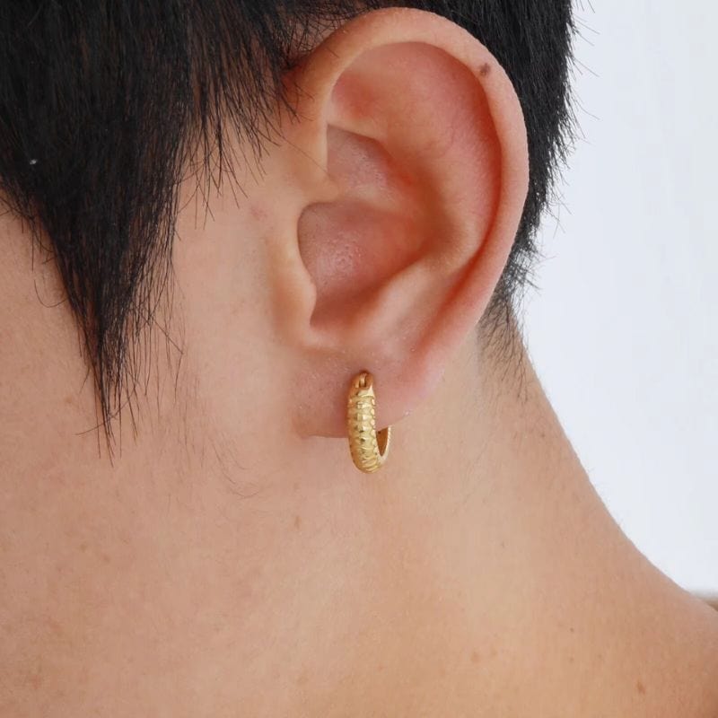 Gros plan sur l'oreille d'un homme portant une boucle d'oreille anneau dorée texturée en acier inoxydable, mettant en valeur le design élégant et masculin du bijou