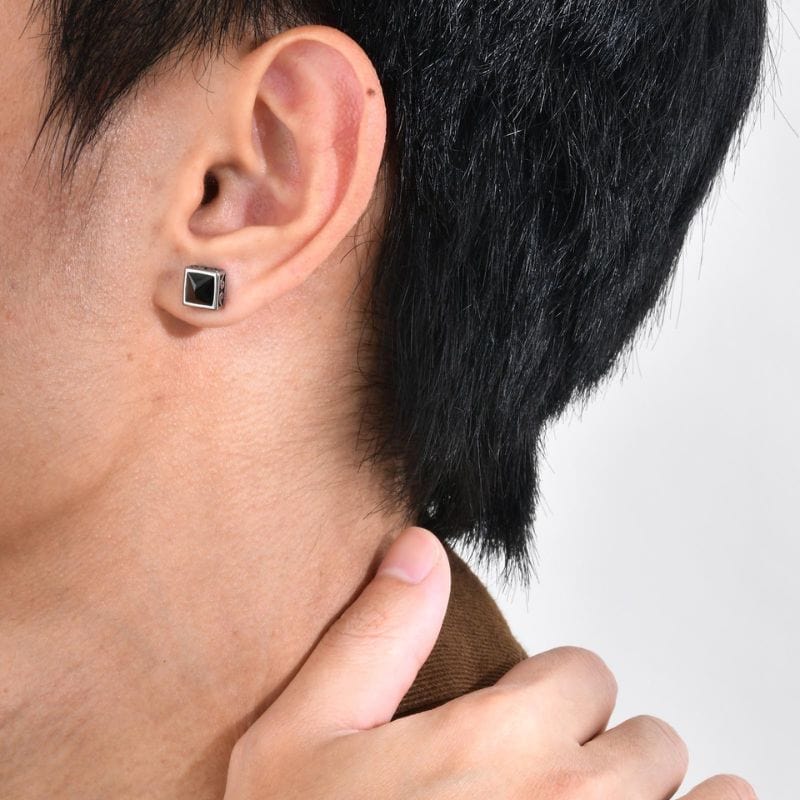 Homme portant une boucle d’oreille clou carrée en acier avec pierre noire, vue zoomée sur l’oreille droite.