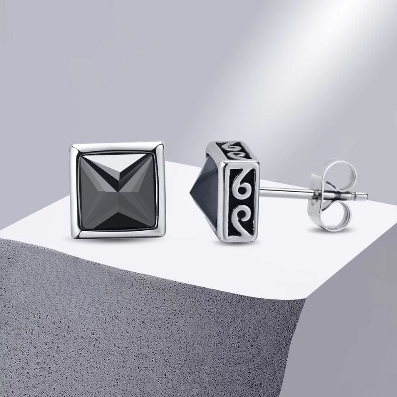 Boucles d’oreilles carrées en acier avec motif gravé sur les côtés et pierre noire centrale, posées sur fond blanc