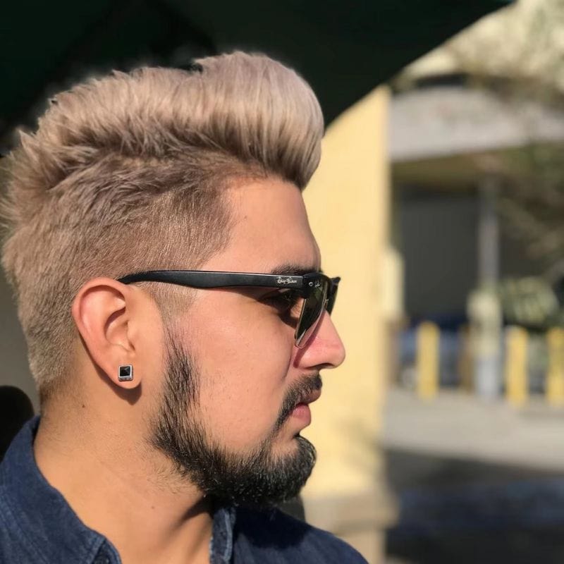 Homme blond avec lunettes de soleil portant une boucle d’oreille carrée noire en acier.
