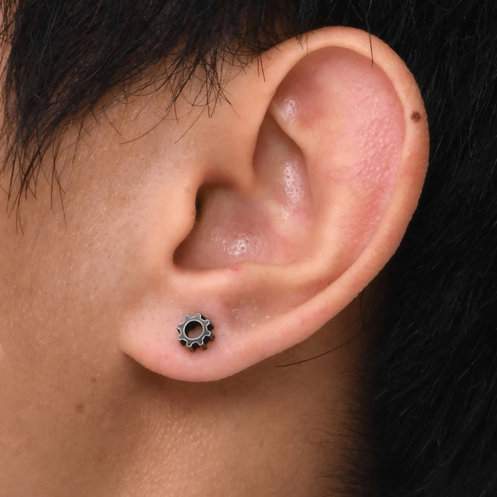Boucle d'oreille acier inoxydable engrenage portée par un homme, style minimaliste