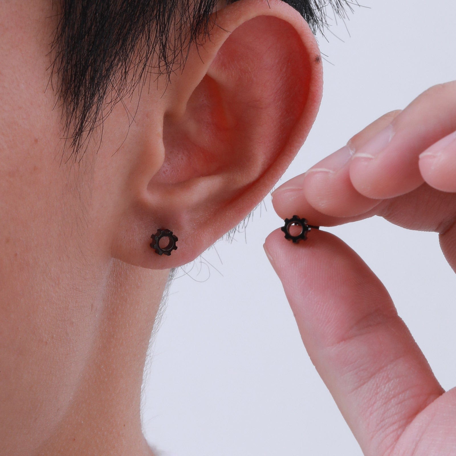 Boucle d'oreille engrenage noir portée par un homme, bijou acier tendance