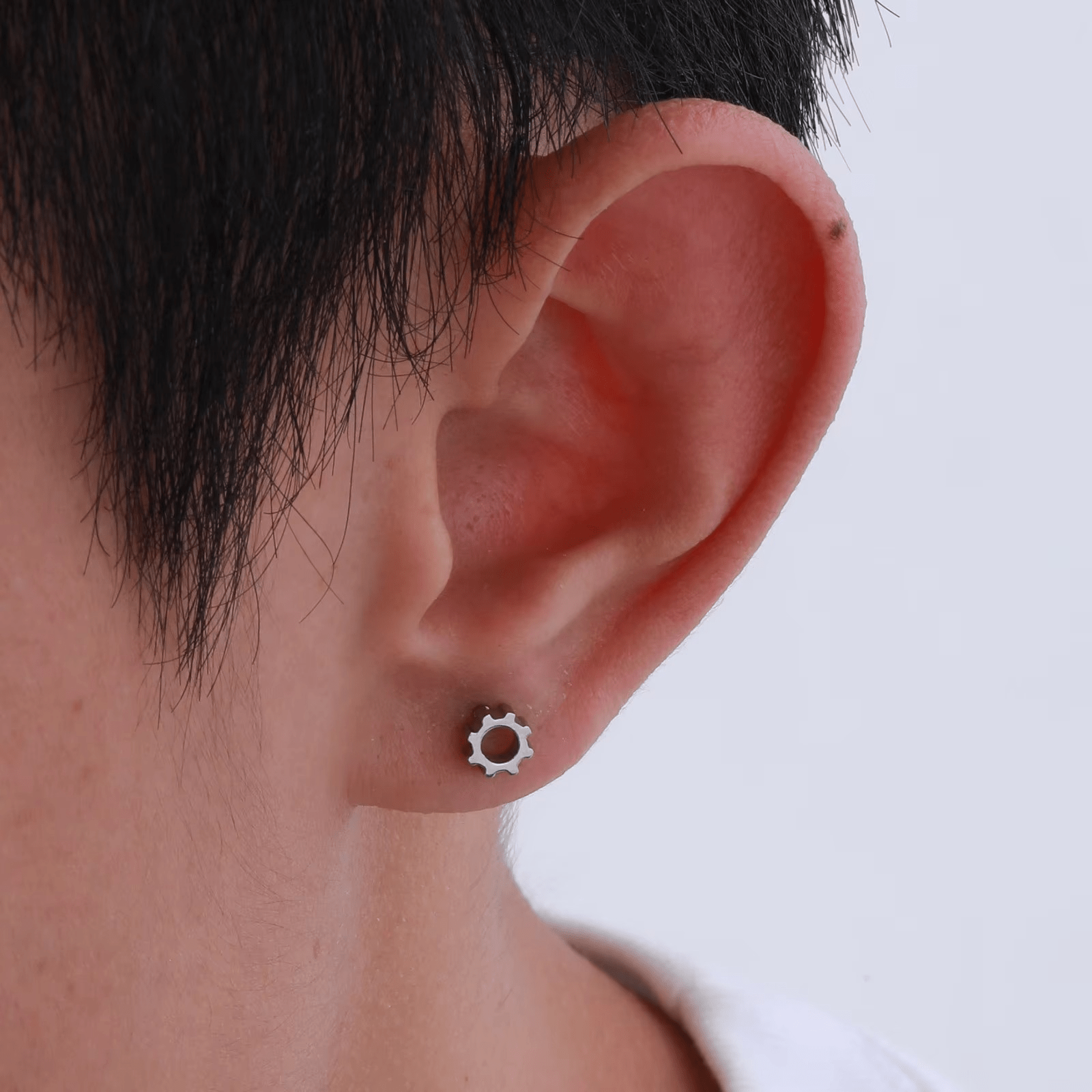 Boucle d'oreille engrenage en acier argenté portée par un homme, look discret