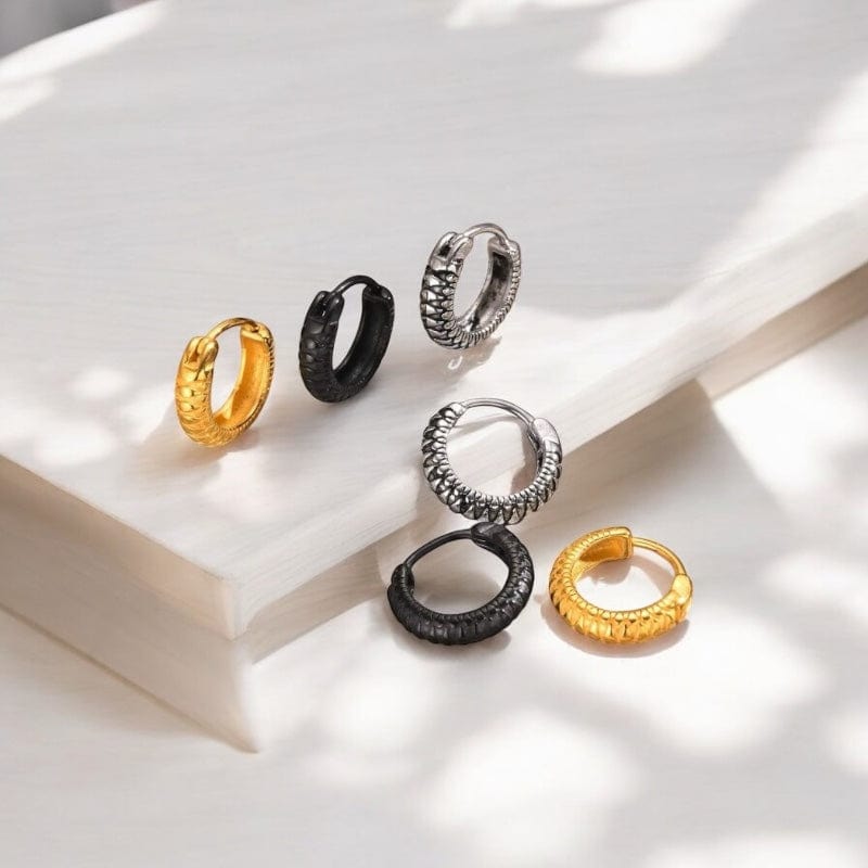 Lot de trois paires d'anneaux créoles pour homme en acier inoxydable effet serpent disponibles en trois couleurs : doré, argenté et noir, disposées élégamment sur un fond minéral.