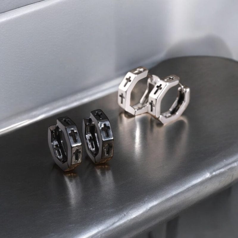 Paire de boucles d’oreilles créoles homme en acier inoxydable noir et argent avec croix gravée, posées sur fond en bois