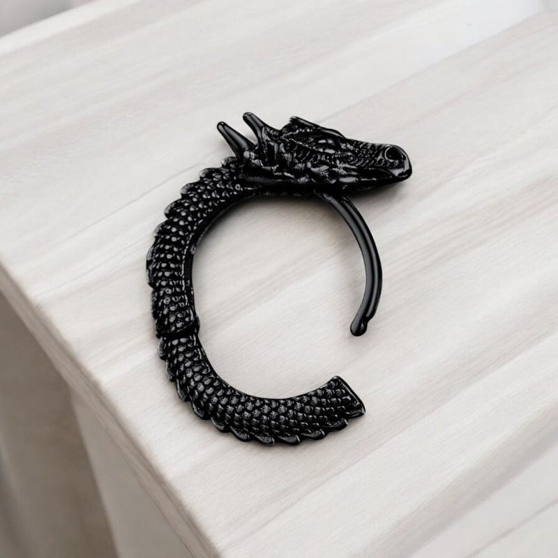 Boucle d’oreille homme dragon noire en acier posée sur une surface