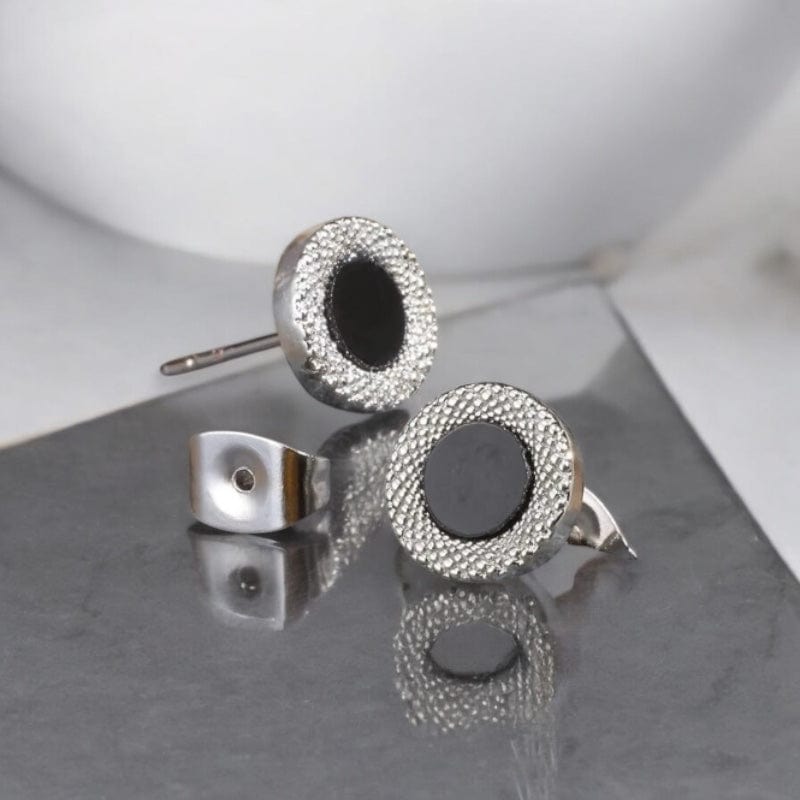Paire de boucles d’oreilles clous pour homme avec cercle noir et contour texturé, posée sur une pierre