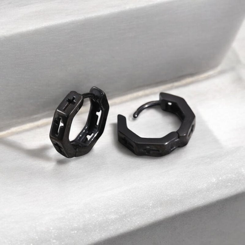 Paire de boucles d’oreilles créoles homme en acier inoxydable noir avec croix gravée – posées sur une pierre naturelle
