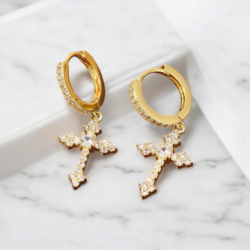 Boucles d’oreilles pendantes croix dorées pour homme posées sur un support en tissu, finition élégante