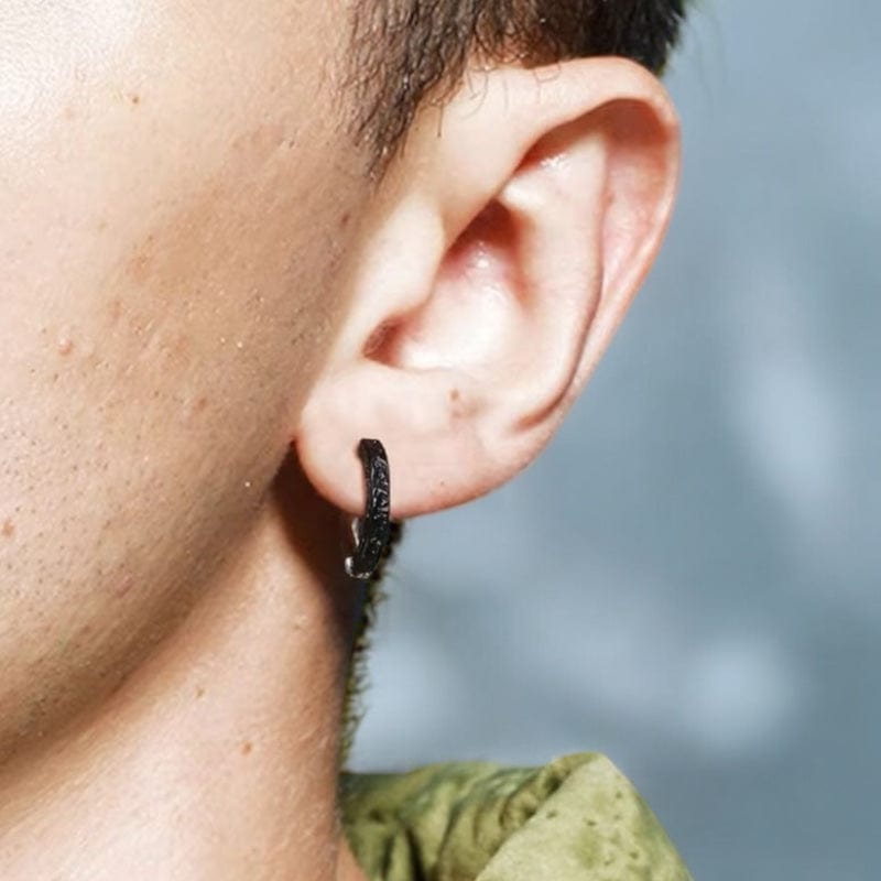 Créole homme en argent plaqué noir et argentée, à motifs texturés subtils, portée par un homme de profil. Anneau sobre et chic idéal pour un style masculin affirmé.