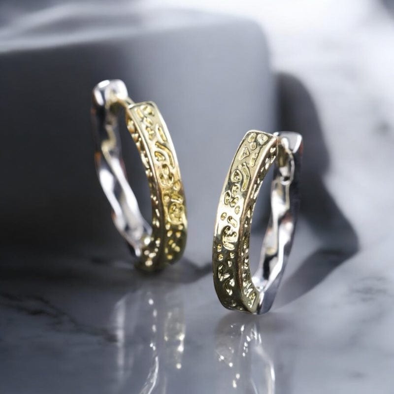 Boucles d'oreilles pour homme de style créole en acier inoxydable bicolore or et argent plaqué, posées sur une surface sombre.