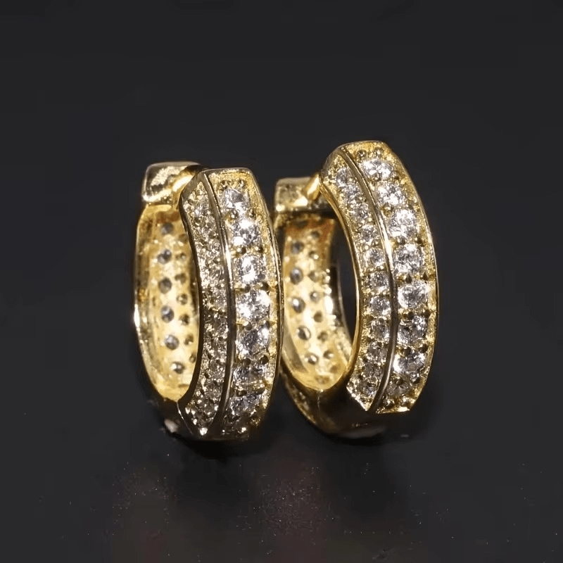 Paire de créoles dorées scintillantes effet diamant sur fond noir, mettant en valeur leurs pierres brillantes.