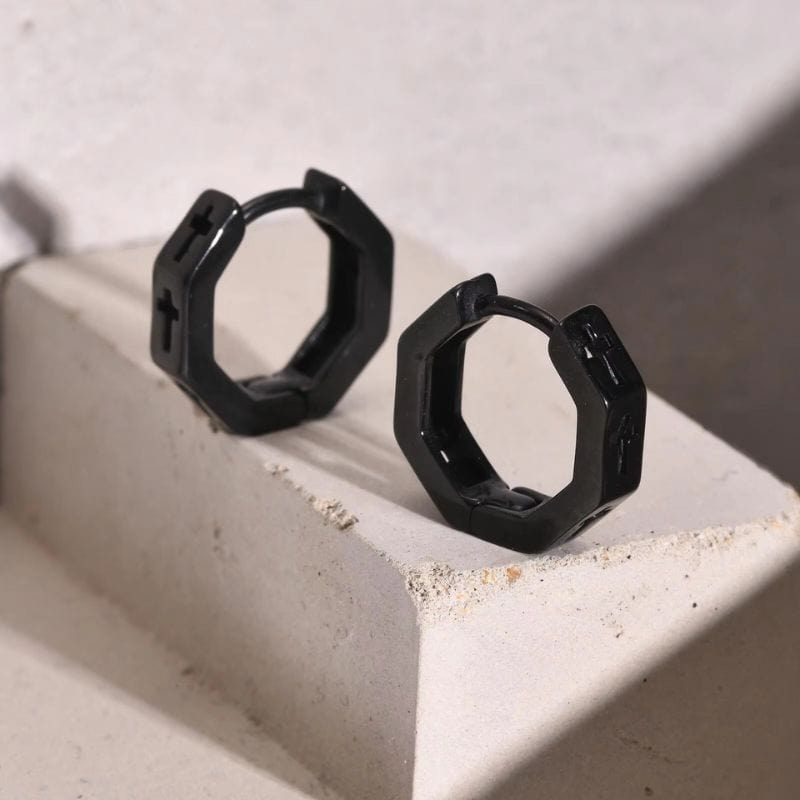 Anneaux créoles homme noirs avec croix gravée – design géométrique en acier inoxydable, posés sur béton