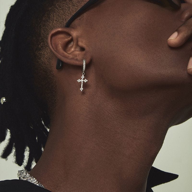 Zoom sur une oreille masculine avec boucle d’oreille croix dorée pendante et strass éclatants