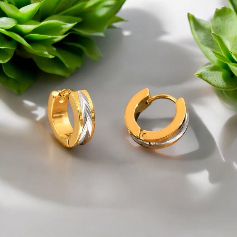 Gros plan sur deux créoles dorées avec motif plume argentée près d’un rocher