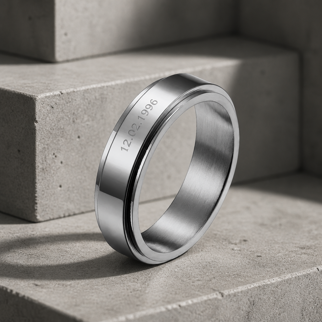Bague homme personnalisée en acier poli, date gravée sur la bande tournante, posée sur du béton