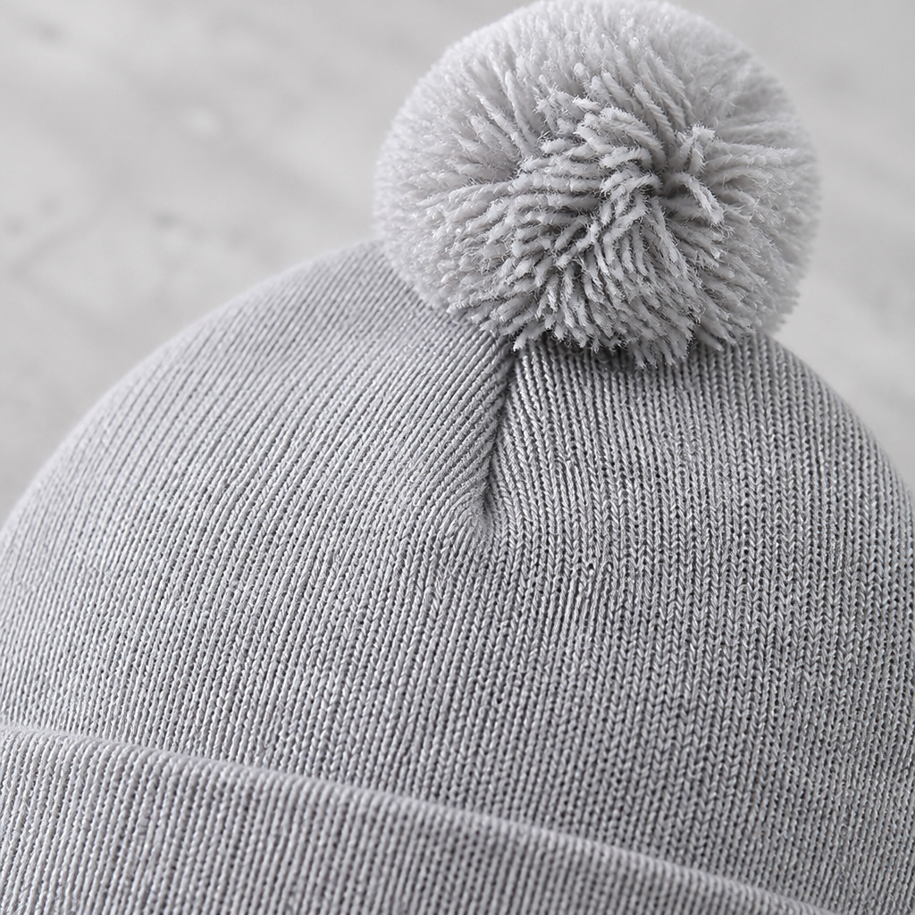 Gros plan sur le pompon et la maille fine du bonnet gris chiné