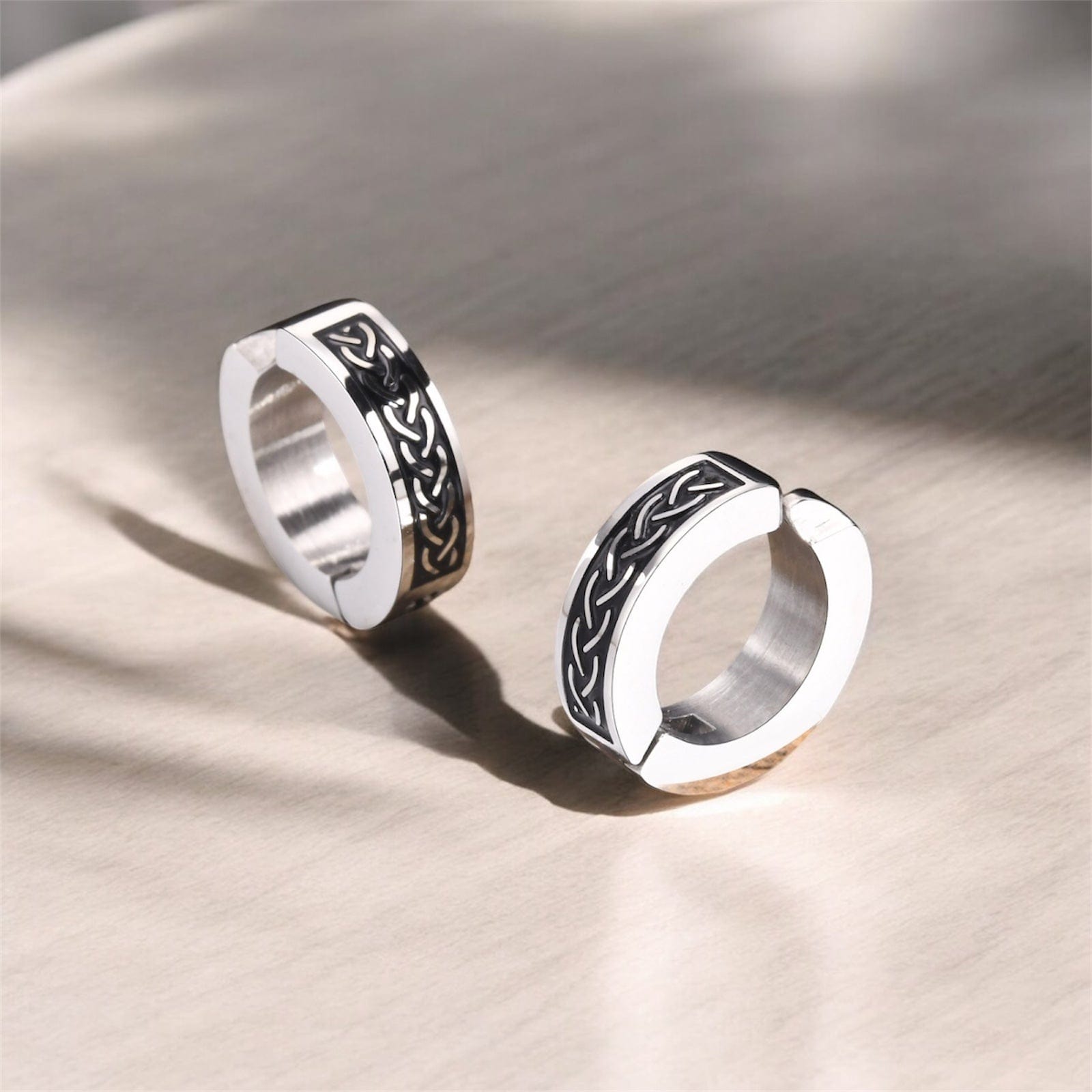 Boucles d’oreilles créoles homme avec gravure celtique, posées sur une surface en bois