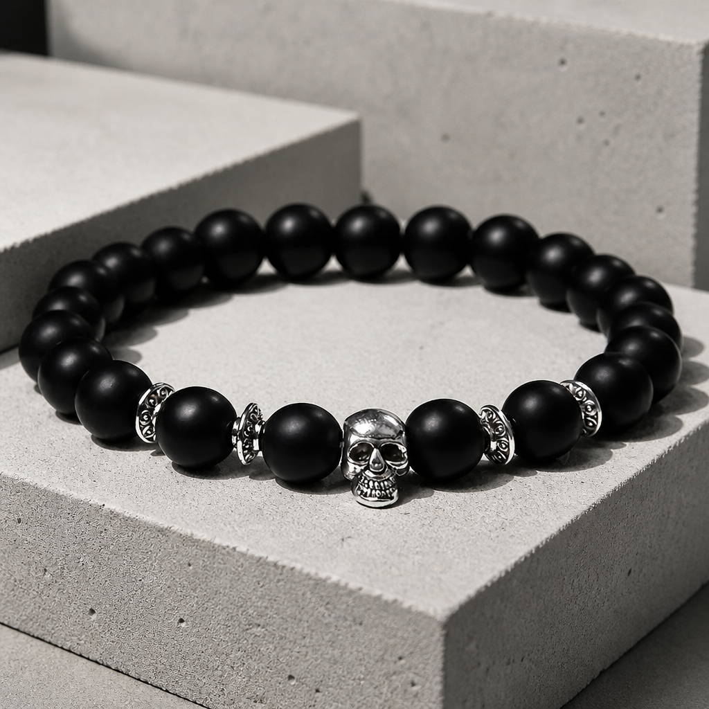 Bracelet homme élastique en perles noires mates, tête de mort argentée au centre, sur un bloc de béton