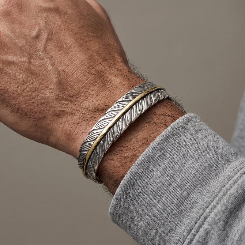 Bracelet plume homme porté au poignet, nervure dorée visible sur le jonc argenté