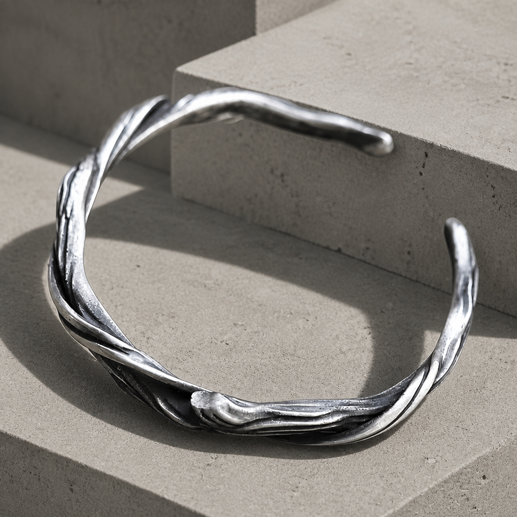 Bracelet torque homme, jonc ouvert argenté au relief sculpté, posé sur des blocs de béton