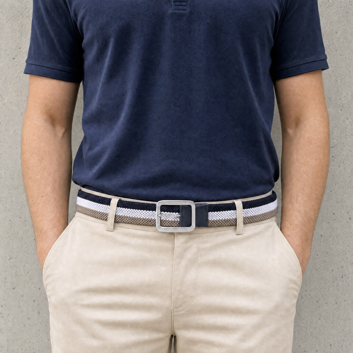 Homme portant la ceinture golf homme tressée rayée bleu marine, blanc et gris taupe avec un polo marine et un chino beige