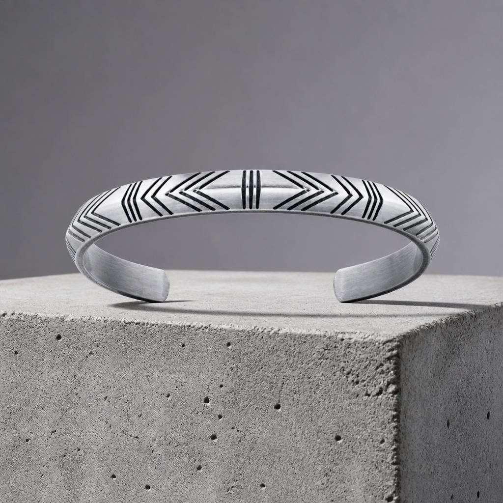 Jonc bracelet homme en acier argent gravé de chevrons, sur bloc de béton