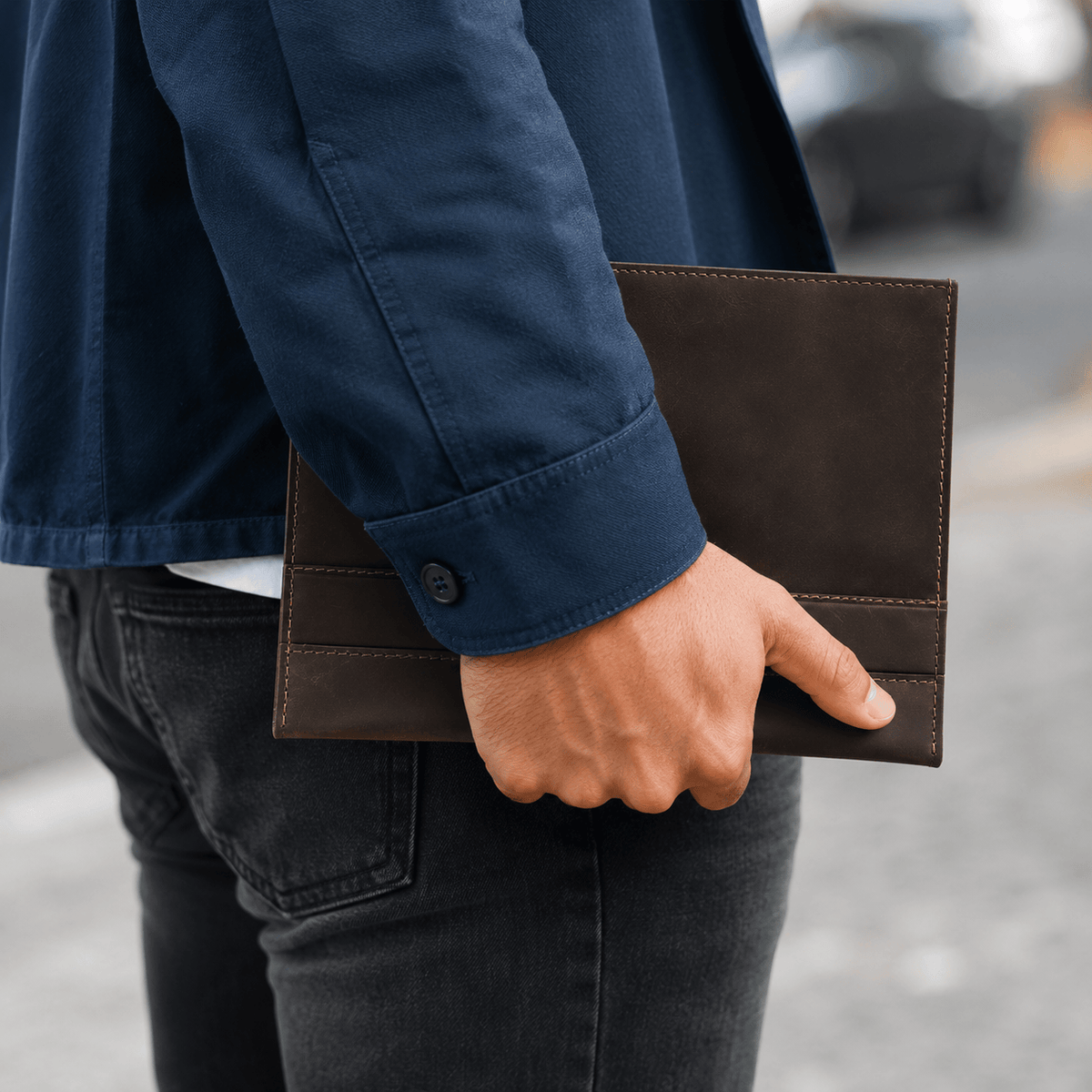 Homme tenant à la main son porte-document A5 en cuir marron dans la rue