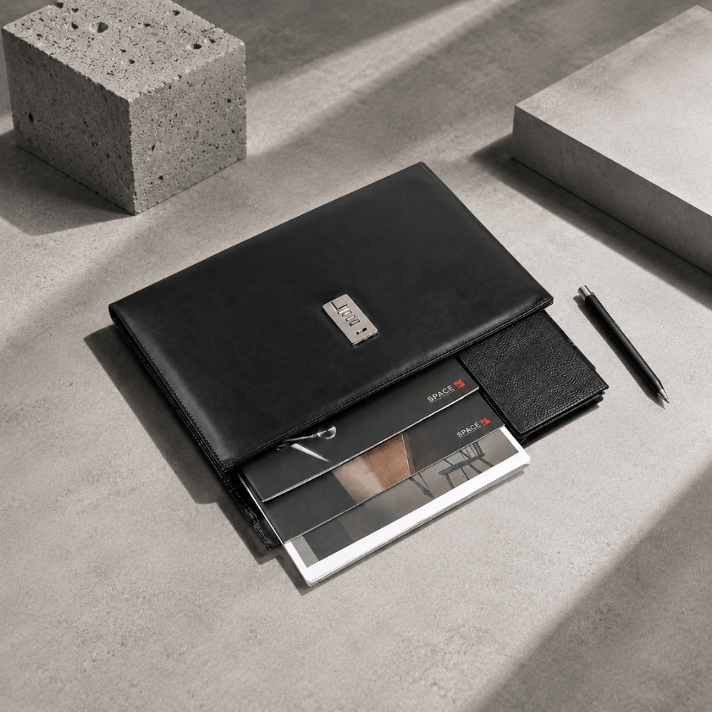 Porte-document noir à code présenté avec magazines, portefeuille et stylo sur béton