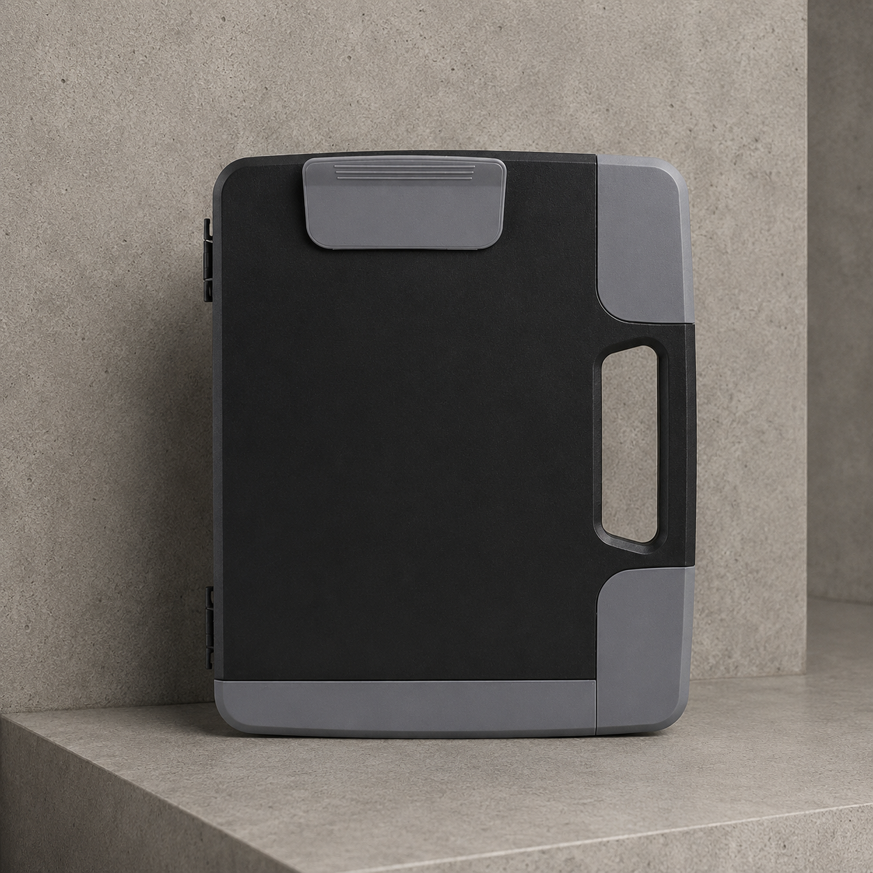 Mallette porte-document de bureau A4 rigide noire à poignée, posée sur béton clair