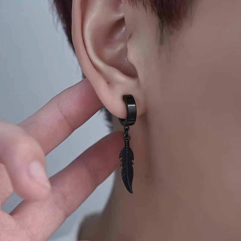 Gros plan sur une boucle d'oreille en acier inoxydable noir, fermoir anneau et pendentif plume