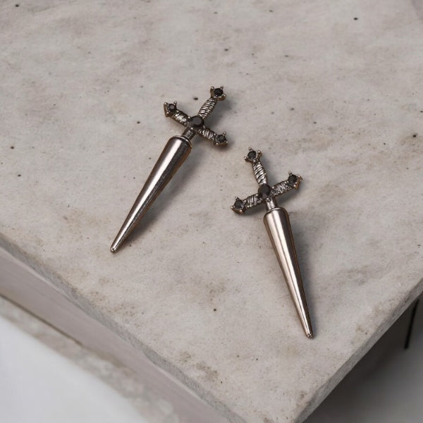 Gros plan sur une paire de boucles d'oreilles épée en alliage de métaux, design gothique avec pierres noires 