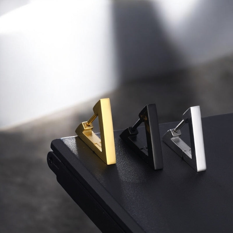 Boucles d’oreilles minimalistes pour homme – Présentation des trois coloris debout sur une surface noire. 