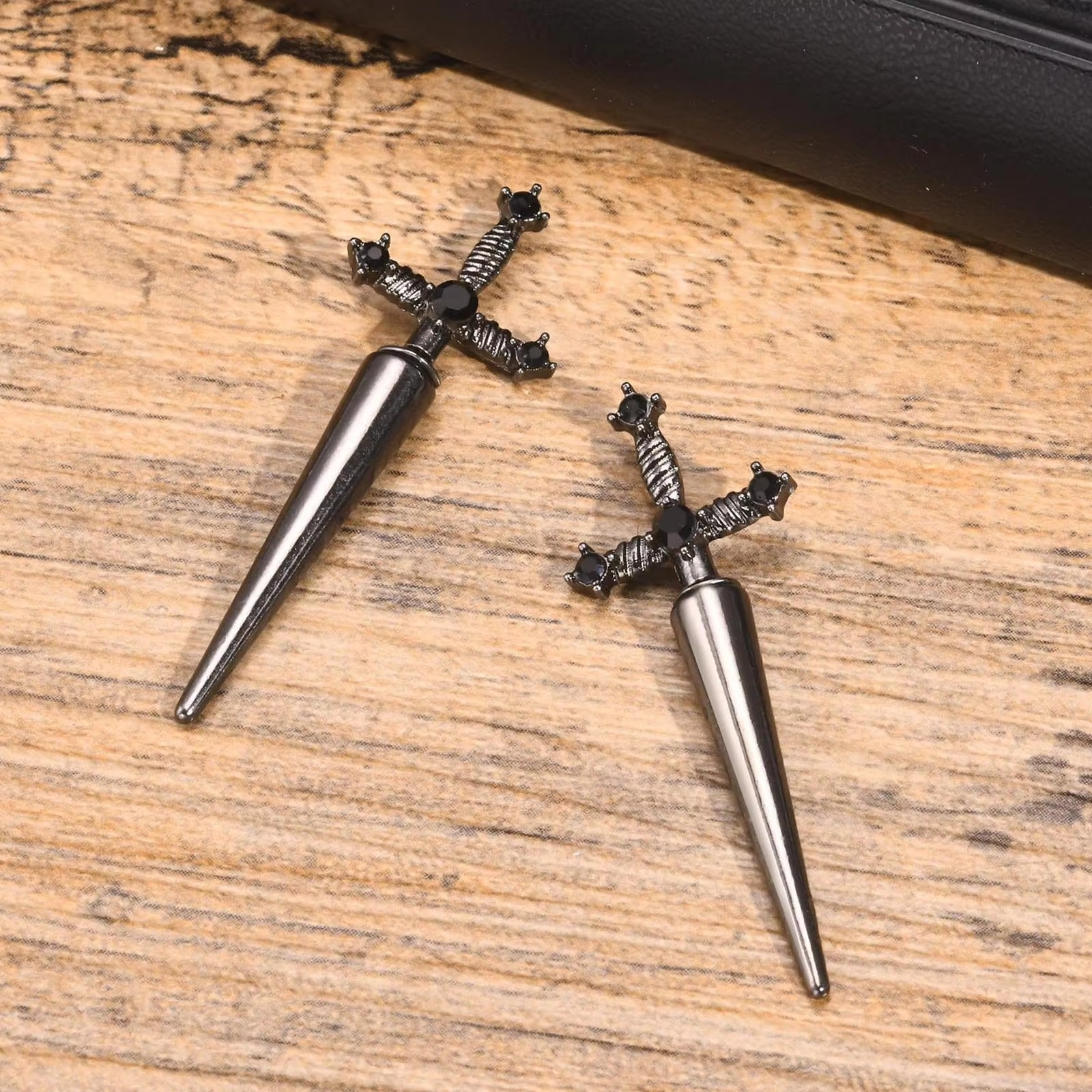 Gros plan sur une paire de boucles d'oreilles épée en alliage de métaux, design gothique avec pierres noires