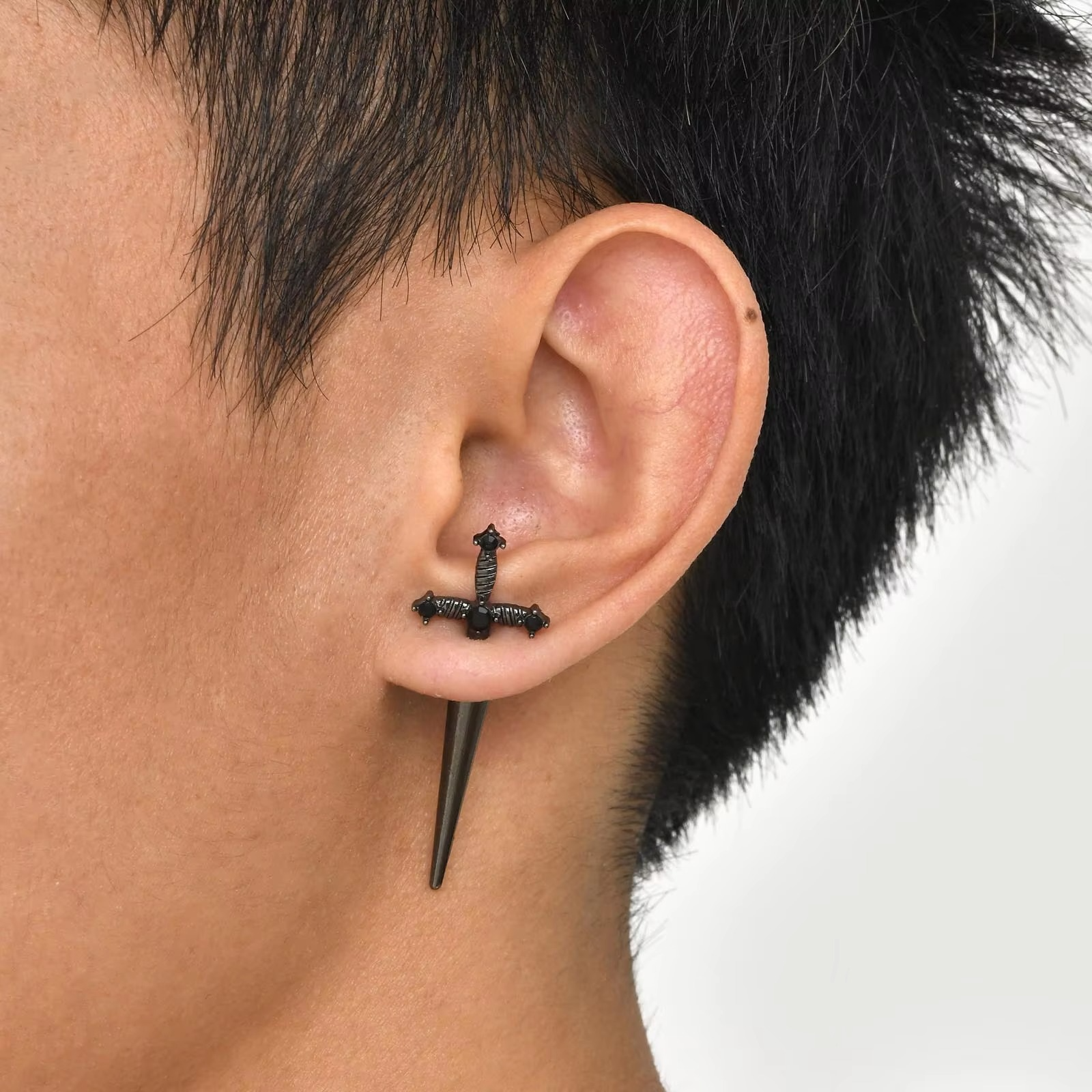 Homme portant une boucle d'oreille en forme d'épée noire, bijou gothique tendance.