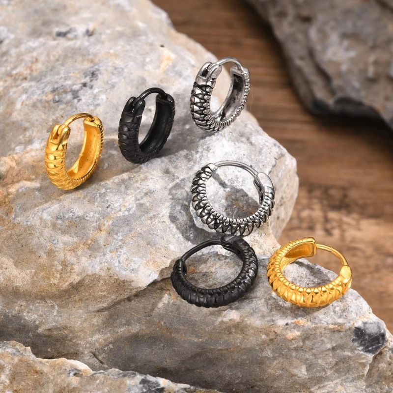 Lot de trois paires d'anneaux créoles pour homme en acier inoxydable effet serpent disponibles en trois couleurs : doré, argenté et noir, disposées élégamment sur un fond minéral.