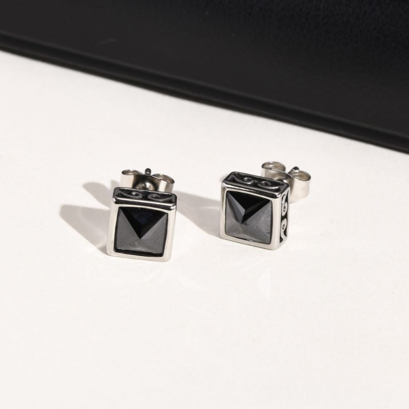 Deux boucles d’oreilles carrées en acier inoxydable ornées d’une pierre noire, posées sur fond blanc.