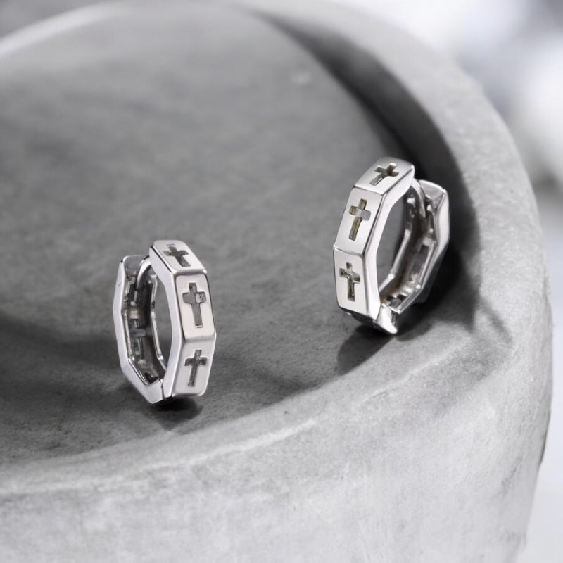 Boucles d’oreilles créoles pour homme en acier inoxydable argenté, motif croix découpée, présentées sur roche foncée 