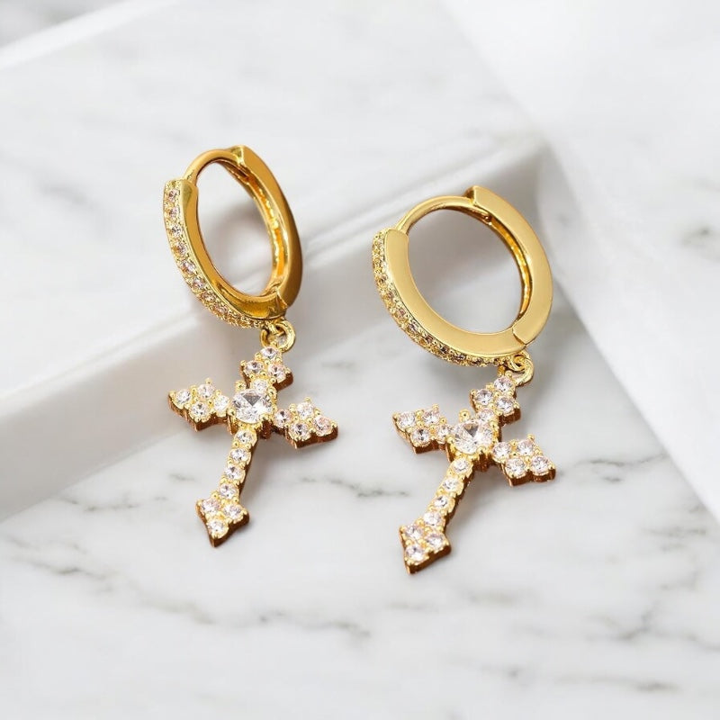 Boucles d’oreilles pendantes croix dorées pour homme posées sur un support en tissu, finition élégante 