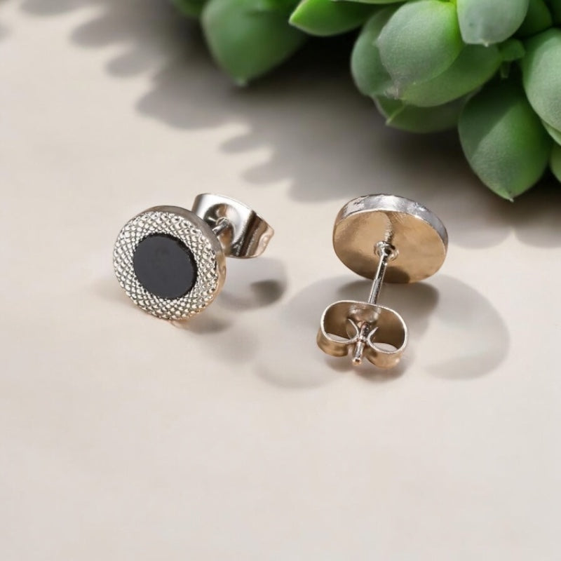 Vue de dessus d’une paire de boucles d’oreilles clous homme avec centre noir et finition métallique 