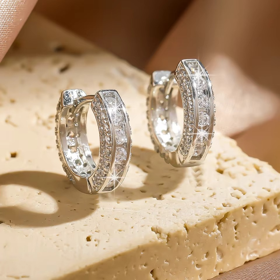 Boucles d’oreilles créoles argentées effet diamant posées sur une surface texturée, captant la lumière.