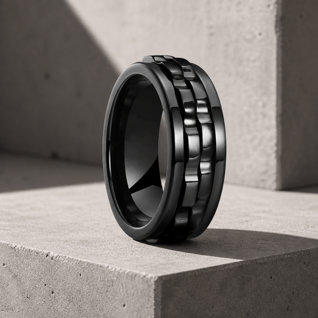 Bague anti-stress noire homme, anneau tournant à maillons noirs, posée sur béton