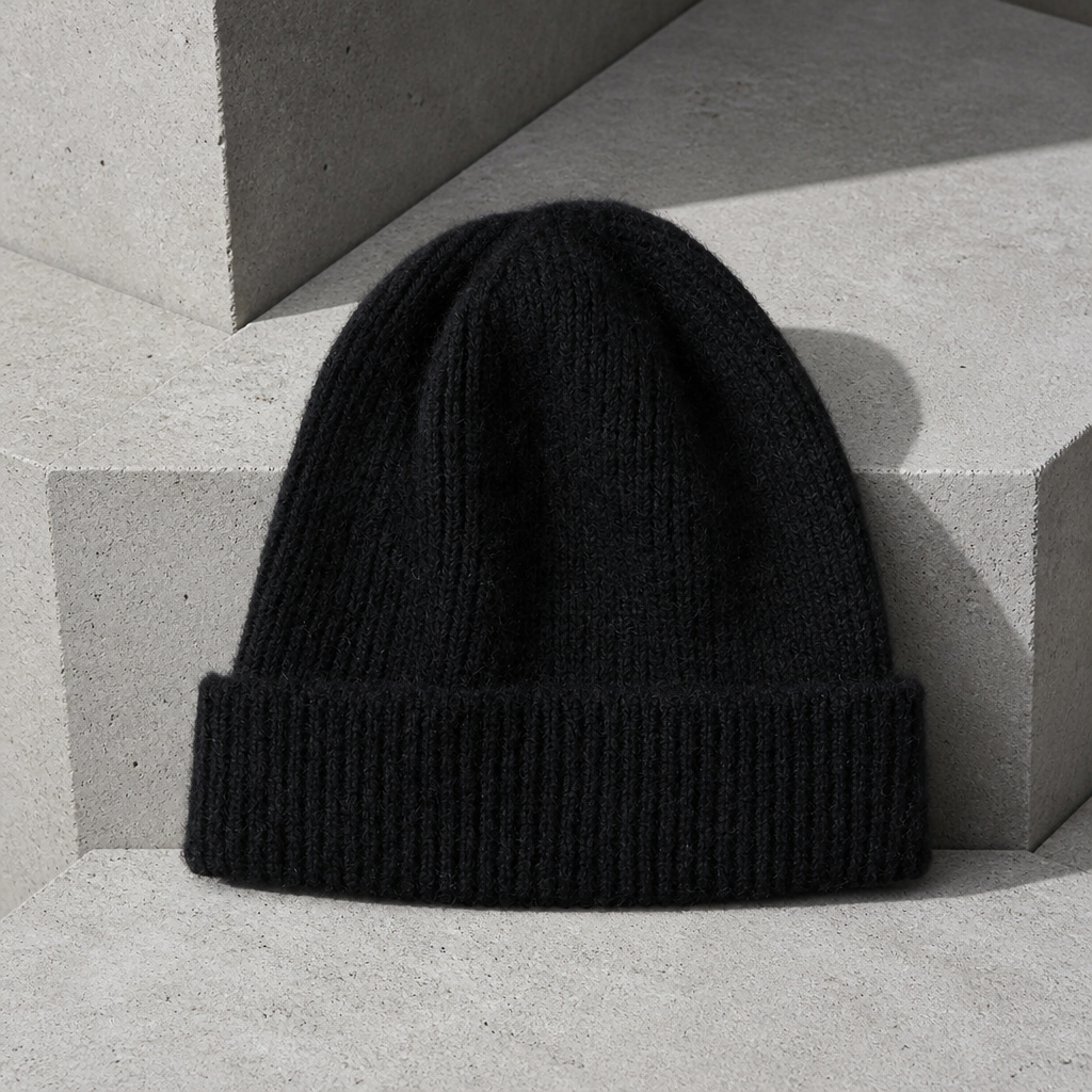 Bonnet en laine homme noir à revers côtelé, posé sur du béton clair