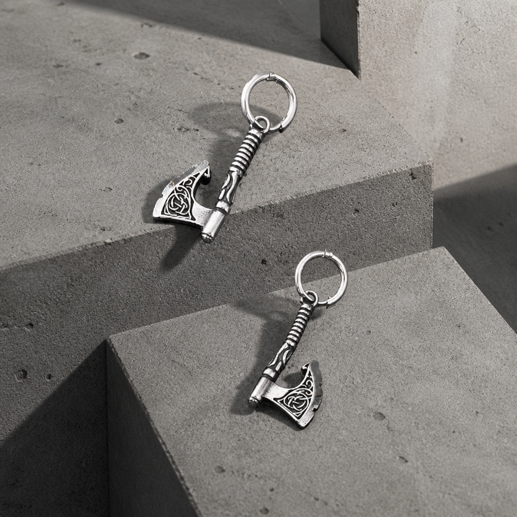Boucles d'oreilles homme en acier inoxydable avec pendentif hache viking, posées sur des blocs de béton