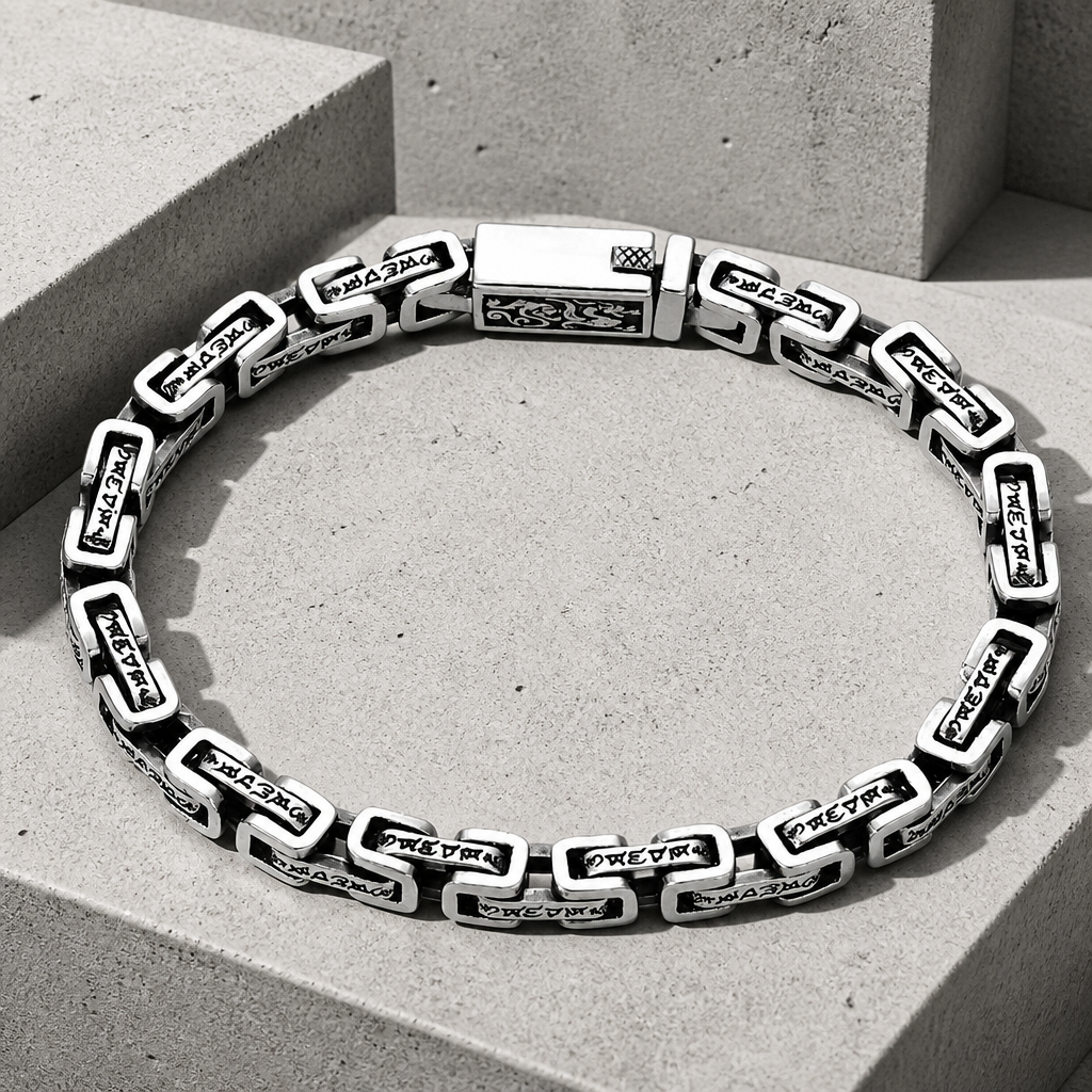 Bracelet bouddhiste homme en argent posé sur du béton, maillons plats gravés